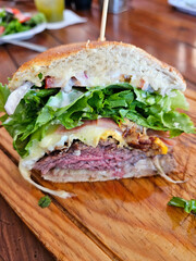 A large Argentinean sandwich with lettuce and cheese on a wooden cutting board. The sandwich is cut in half and is placed on a table