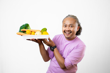 Asian long-haired man looks happy and confident carrying a tray of fruits and vegetables