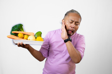 A long-haired Asian man looks disgusted and disgusted with a tray of fruit and vegetables that he...