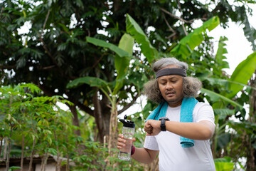 A long-haired Asian man is jogging in the morning while occasionally looking at his watch