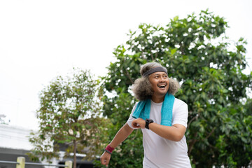 Fototapeta premium a long-haired asian man is jogging in the morning while swinging his towel up looking confident and happy