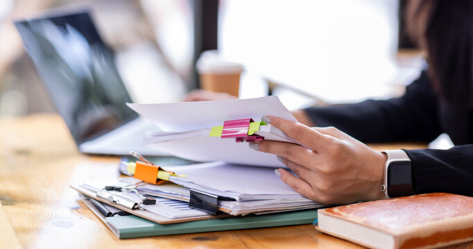 Business asian woman Reviewing Documents, business woman's hands meticulously reviewing a stack of documents, highlighting the details and precision of her work. 
