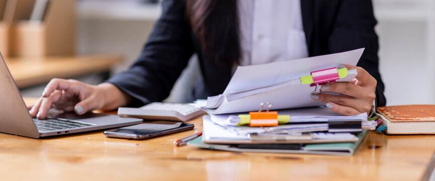 Business asian woman Reviewing Documents, business woman's hands meticulously reviewing a stack of documents, highlighting the details and precision of her work. 
