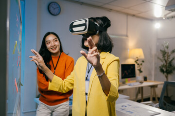 Two businesswomen are brainstorming using a whiteboard and virtual reality glasses in their office. They are smiling and having fun while working on this innovative project