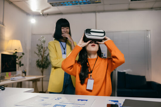 Two young businesswomen working in a modern office, one of them is wearing a vr headset and experiencing virtual reality - Powered by Adobe
