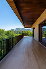 Modern balcony overlooking lush green trees and mountain landscape during bright daytime