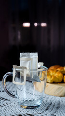Glass cup with an open coffee filter ready for brewing on a table next to bread rolls