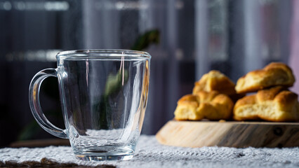 Empty glass cup next to bread rolls on a wooden tray in an indoor setting