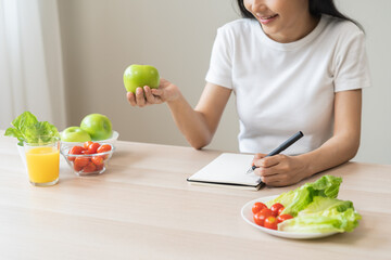 Diet, happy asian young woman working, write diet plan right nutrition holding green apple with eat fresh vegetable salad is food for good health. Nutritionist for weight loss of healthy at home.