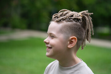 A 10-year-old boy with dreadlocks and African braids on his head. Summer green background. © Tatyana Orakova Орак