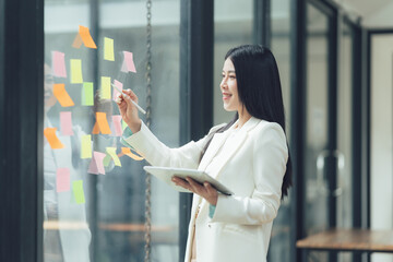 Strategic Vision: A young businesswoman plans her next move, using sticky notes and a tablet. Her focused expression and bright workspace convey intelligence and innovation.