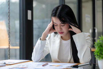 The Weight of Responsibility: A young businesswoman sits at her desk, deep in thought, her hands...