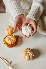 Handmade wax candle in the shape of pumpkins in the hands of a girl