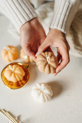 Handmade wax candle in the shape of pumpkins in the hands of a girl