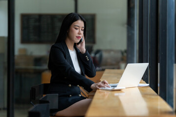 Businesswoman on Phone Call: A focused young businesswoman in a black blazer sits at a wooden table...
