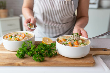 Homemade vegetable soup with meatballs in a bowl on kitchen counter. Served by a woman with apron 