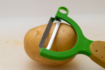 a potato peeler resting on a potato on a white veined marble table
