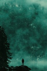 Fototapeta premium A solitary figure stands on a rock overlooking a misty lake and a forested mountainside.