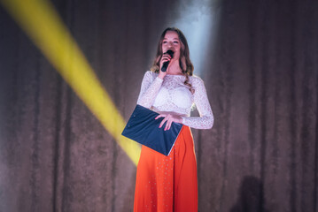 A girl hosting a concert with a microphone on stage in the spotlight.