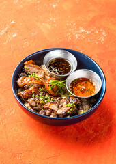 Garlic Rosemary Chicken Rice Bowl with Sauces and Green Onion isolated on orange background side view of Appetizer Meal