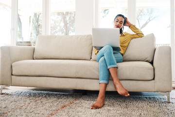 Obraz premium Woman, home and laptop on sofa with browsing internet for entertainment, news and streaming service. Female person, apartment and relax on couch in living room for fibre connection and subscription