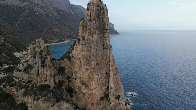 Pull in drone shot of Pedra Longa rock in Sardinia ending with a close up of wild goats climbing high on the rock