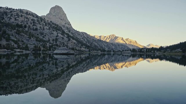 Mountain reflection on calm Rae Lakes during golden hour, surrounded by rocky peaks and forest
