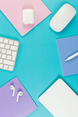 Top view of white keyboard, mouse, touchpad, earphones case, pen on blue background. Purple, pink and blue notebooks, modern office, school. Flat lay, copy space.
