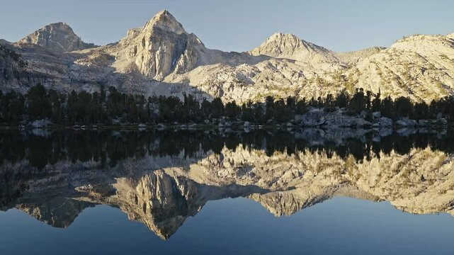 Majestic mountains and trees reflect perfectly on the still waters of Rae Lakes at sunrise