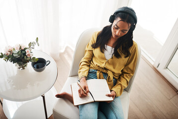 Woman, home and wiring on diary with headphones for music, audio or podcast on chair. Female...