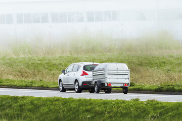 Car towing trailer along bright rural route