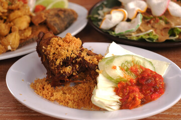 Fried duck with fried flour crumbs, cucumber slices, cabbage and chilies served on a white plate