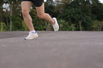 Fototapeta premium Low angle shot sportsman legs in sport shoes jogging along a paved road. Fitness and active lifestyle