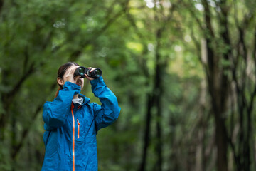 Young explorer in a blue jacket observing the forest with binoculars, enjoying birdwatching and...