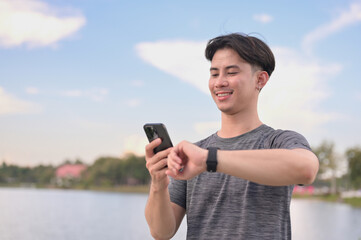Smiling male runner syncing fitness data on his mobile phone and smartwatch