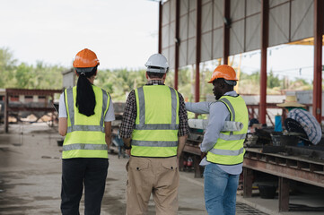 Multi-ethnic workers wearing hard hats in Engineering Workshop. Three industrial workers in hard hats are conversing on the storeroom floor.