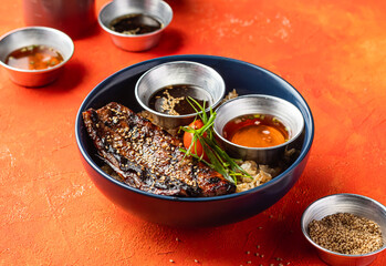Teriyaki Grilled Bangus Belly Rice Bowl with Dipping Sauce and sesame seeds isolated on orange background side view of fast food meal