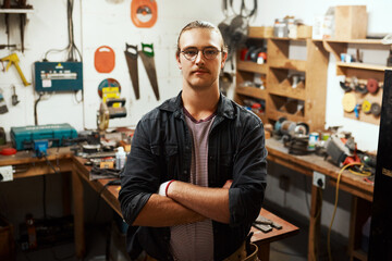 Fototapeta premium Man, portrait or carpenter with confidence at workshop for woodwork, skill or talent in garage. Young, male person or professional artisan with arms crossed for timber, funiture or carpentry business