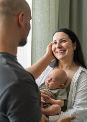 Family with newborn baby boy. Parents gently touching baby and each other. Baby is lying quietly in their arms. Warmth and harmony in family. Care and happiness.