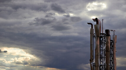 Petrochemical chimneys discharge devices over dramatic sky. Industrial cloudscape 16x9 with...