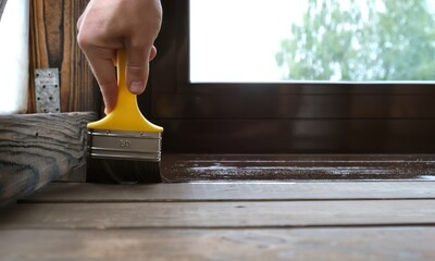 Close-up of a brush painting wood floor in brown color. Wood plank impregnation. Finish oil coating of board. Second layer of oiling. Manual construction work in a gazebo. Natural building materials