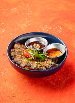 Korean Grilled Pork Belly Rice Bowl with dipping sauce with herbs isolated on orange background side view of fast food meal