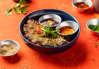 Korean Grilled Pork Belly Rice Bowl with dipping sauce and sesame seeds isolated on orange background side view of fast food meal
