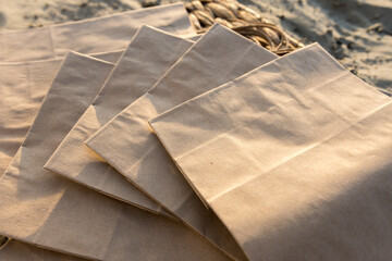 Eco-friendly paper bags with twisted handles lying on a sandy surface. Ideal for themes of...