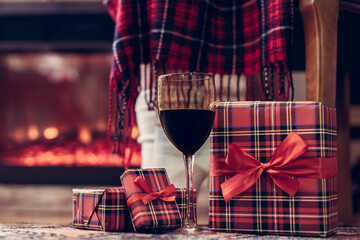 Legs of disabled woman in a socks covered plaid sitting and relaxation on armchair near fareplace and christmas tree with glass of wine after finishing pakking gift boxes for family. Bottom view.