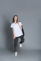 A young girl dressed in a white t-shirt and jeans stands casually with her jacket thrown over her...