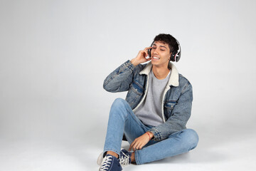 Chico con jeans y camiseta blanca ajustando auriculares  sobre fondo blanco., escuchando música y...