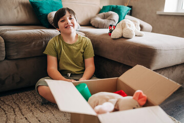 Happy cheerful kid boy packing his toys for delivery donation box. Charity and recycling