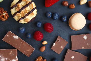 Macarons, chocolate, cookies, berries and various nuts on dark blue background. Top view.