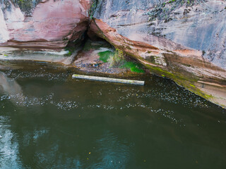 Log floating in the water on the Gauja River near a sandstone cliff, photo view from a drone.